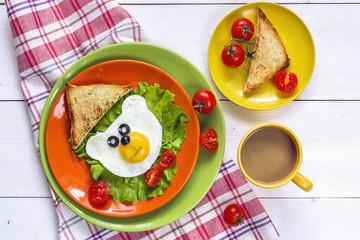 Funny Breakfast with bear-shaped fried egg, toast, cherry tomato, lettuce on colored plates and coffee.