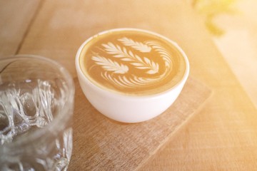 cup of hot milk coffee with beautiful latte art and glass of water on wooden table, morning light