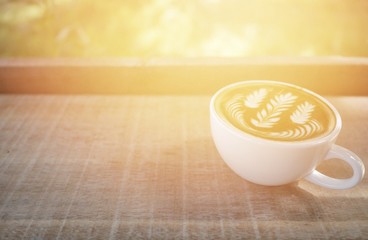 cup of hot milk coffee with beautiful latte art on wooden table, morning light
