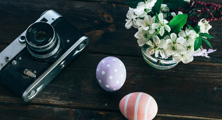 Preparation for Easter. Colorful handmade Easter eggs, paint, retro camera and vase with flowers on a wooden background