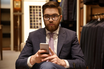 Fototapeta na wymiar Serious man in suit and eyeglasses holding mobile phone