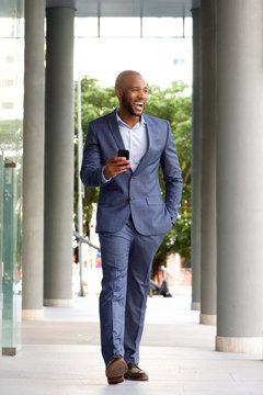 Full length handsome african businessman walking with mobile phone