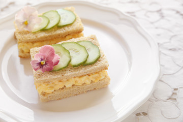 Obraz na płótnie Canvas Egg and cucumber afternoon tea sandwiches with edible flowers, toning