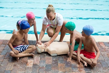 lifeguard giving rescue training to children at poolside
