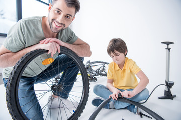 Fototapeta na wymiar Son and father repairing bicycle tire in studio on white