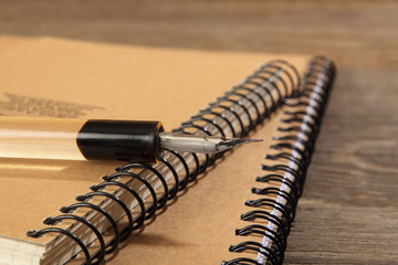 The old penholder with the pen lies on the notebooks sewn with metal springs on a wooden table....