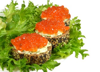 Three small sandwiches of black baguette with grains of cereals and poppy seeds, with red caviar and butter, knocked down with finely chopped dill, lie on green leaves of crispy leaf lettuce. Isolated