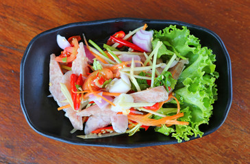 Thai sour pork sausage salad in black plate on wood table