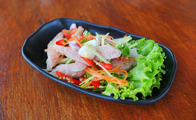 Thai sour pork sausage salad in black plate on wood table