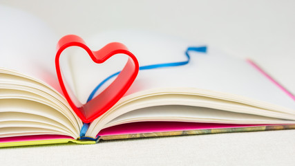 Red heart over diary book with bookmark on white table