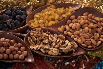 Large collection of nuts, seeds and dried fruits in brown wooden bowls isolated on a golden background