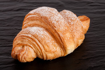 one croissant on black stone background closeup