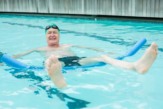 Cheerful mature man swimming with pool noodle