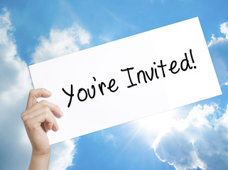 You're Invited! Sign on white paper. Man Hand Holding Paper with text. Isolated on sky background