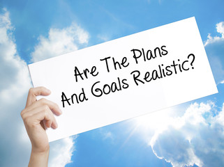 Are The Plans And Goals Realistic? Sign on white paper. Man Hand Holding Paper with text. Isolated on sky background.