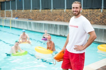 Male lifeguard standing while swimmers swimming in pool