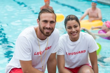 Male and female lifeguards crouching at poolside - obrazy, fototapety, plakaty