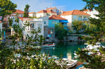 Fototapeta na wymiar Cozy picturesque town of Bozava, Dugi otok, Croatia. Small colorful houses near emerald green water where boats and yachts are floating. Everything framed with lush green foliage.
