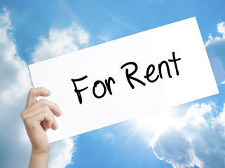 For Rent Sign on white paper. Man Hand Holding Paper with text. Isolated on sky background