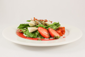 Mix of hot sausages with bacon on a cushion of lettuce leaves, in a duet with parmesan and strawberries, garnished with pumpkin seeds, dressed with raspberry sauce