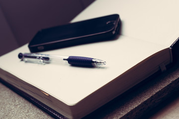 Empty notebook, mobile phone and a pen on wooden table