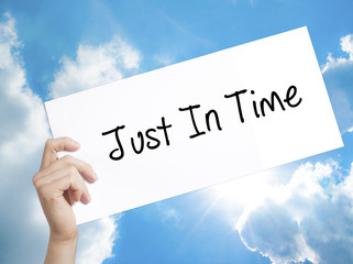 Just In Time Sign on white paper. Man Hand Holding Paper with text. Isolated on sky background