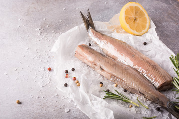 Freshly salted herring with salt, lemon ans rosemary on gray background with copy space. Traditional Dutch delicacy. Retro style toned.