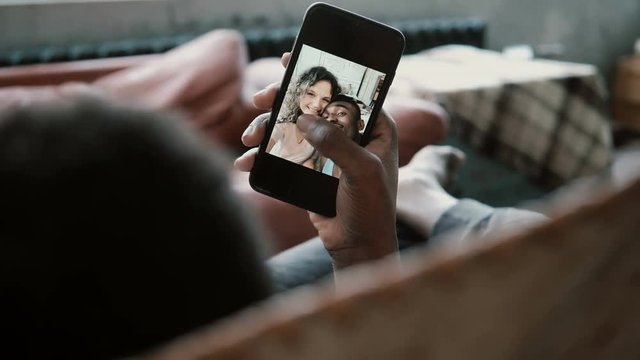 African man uses Smartphone, looks at photos with Caucasian girlfriend. Man and woman kissing, smiling and laughing.