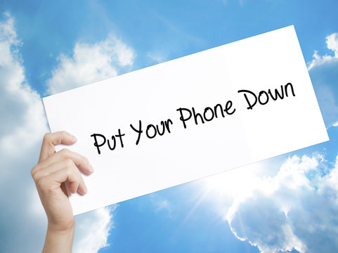 Put Your Phone Down Sign on white paper. Man Hand Holding Paper with text. Isolated on sky background
