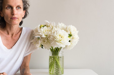 Middle aged woman with grey hair looking thoughtful leaning on table with white dahlias (cropped)