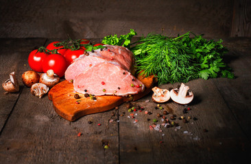 Raw juicy meat steaks ready for roasting on a black chalk board. Fillet with cherry tomatoes, hot pepper and herbs. Space for text