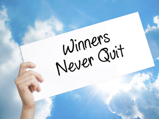 Winners Never Quit Sign on white paper. Man Hand Holding Paper with text. Isolated on sky background