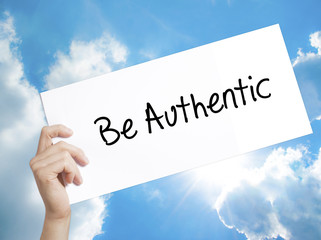 Be Authentic Sign on white paper. Man Hand Holding Paper with text. Isolated on sky background