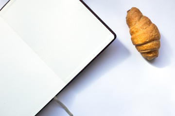 Fresh croissant and notepad on white backgroud. Top view with copy space