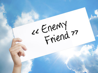 Enemy - Friend Sign on white paper. Man Hand Holding Paper with text. Isolated on sky background.