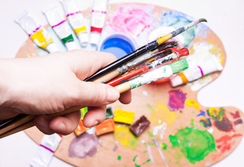 Female hand holds brushes over colored paints