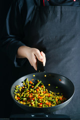 Cooking of vegetable mix stew with tossing on a hot frying pan. Colorful grains of corn and peas, asparagus and sweet peppers.