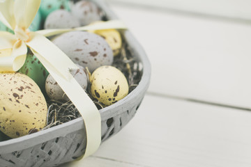 Basket filled with colored Easter eggs with a yellow ribbon on white wooden background