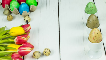 Bouquet of tulips, painted Easter eggs, quail eggs and eggs in egg cups on white wooden background with free text space