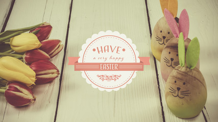 Bouquet of tulips and three colorful Easter Bunnies on white wooden background with label saying have a very happy easter