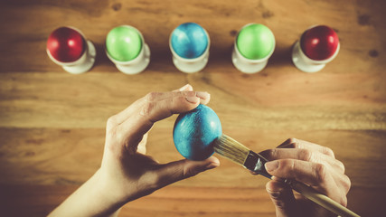 Woman hands painting Easter eggs on a brown wooden table