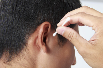   Young man cleaning ears with cotton pud stick on white background.