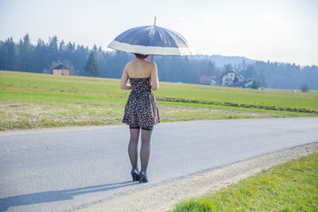 A young woman is standing in the middle of the street with a summer umbrella in her hands.