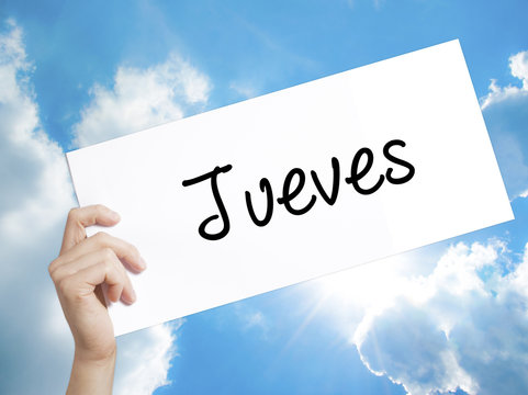 Jueves (Thursday in Spanish) Sign on white paper. Man Hand Holding Paper with text. Isolated on sky background