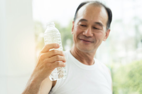 Close up Asian senior man holding bottle of water at a gym. Drinking water. Tired, thirstily. freshness.