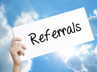 Referrals Sign on white paper. Man Hand Holding Paper with text. Isolated on sky background.