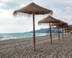 Straw parasols on empty beach. Nerja, Spain