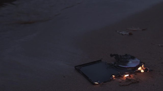 data cd dvd laser compact disc case on fire on the wet sand at coast HD