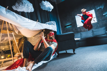 father and son in red superhero costumes playing at home