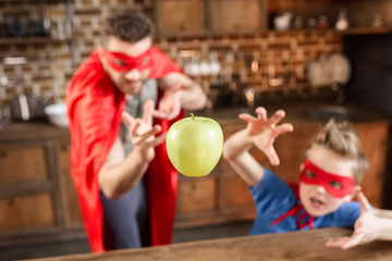 father and son in red superhero costumes playing with apple
